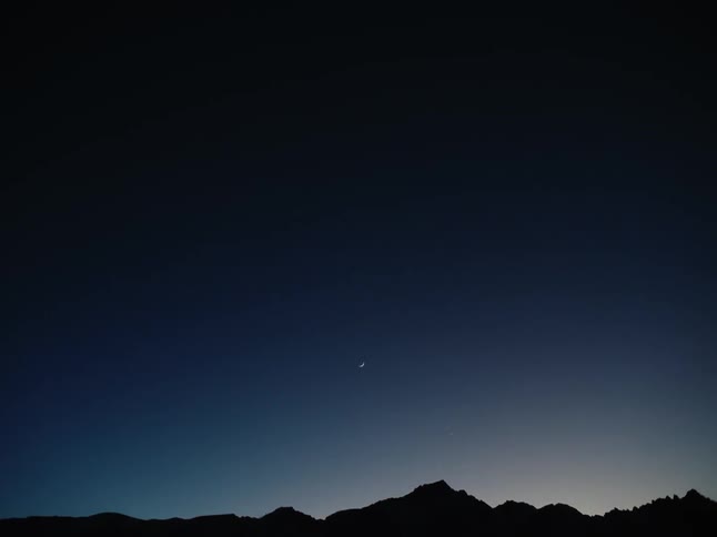 A silhouette of a mountain range on a very dark morning with the moon in the sky