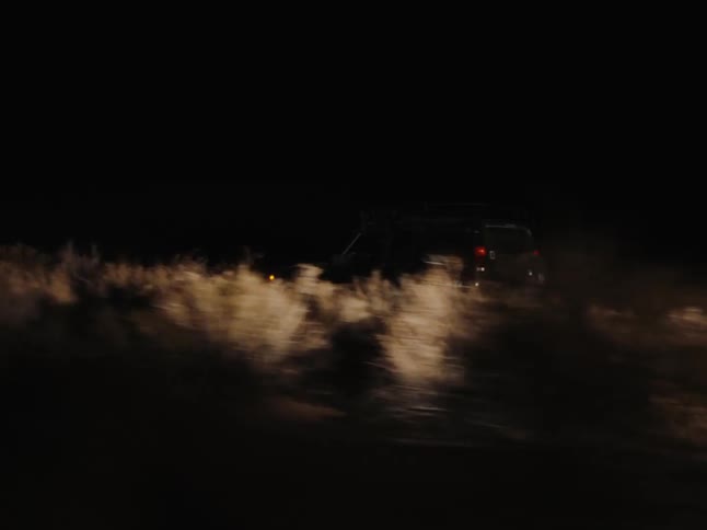 A black jeep driving down a country road in a field at night