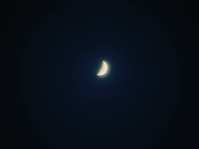 A crescent moon stands out in the dark night sky emitting a soft white glow