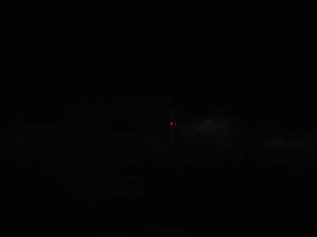 A vehicle races down a road in nature at night