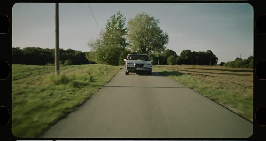 Driver weaves back and forth on road passing field before turning at intersection while passenger waves out car window
