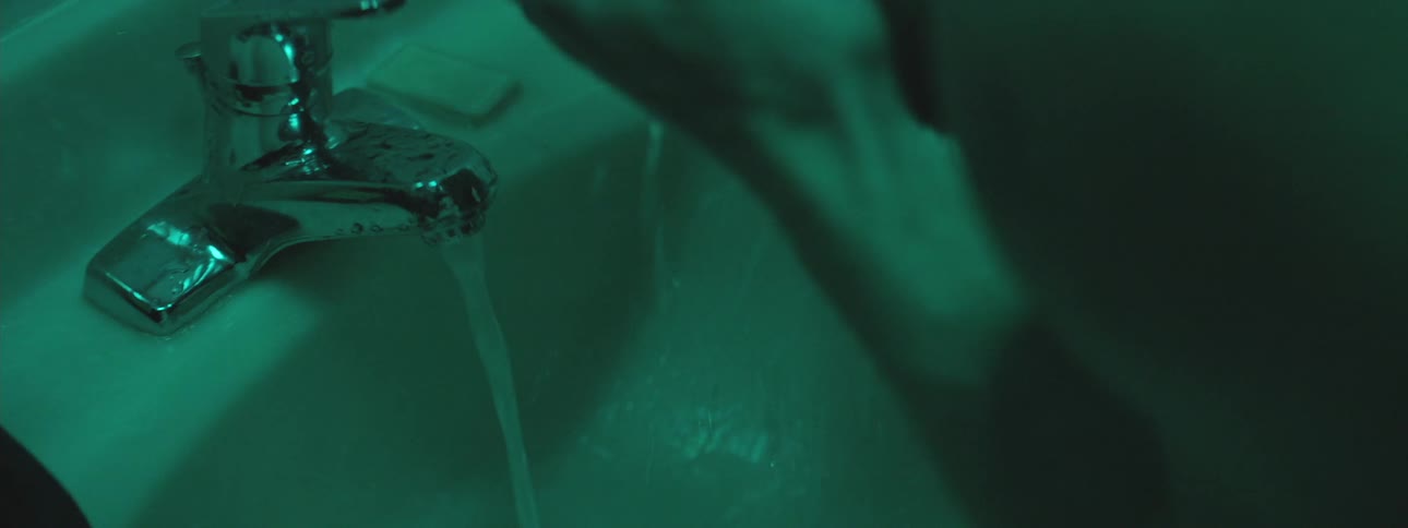 A person washing his hands and face on the bathroom under a green light