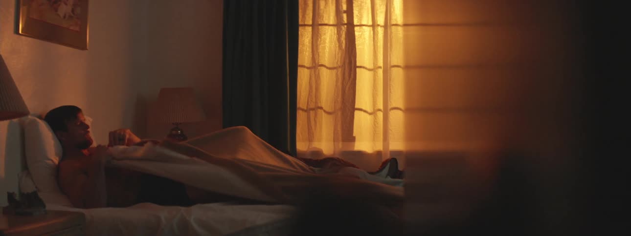 Man lying on the bed in a dimly lit bedroom pulls the covers over himself