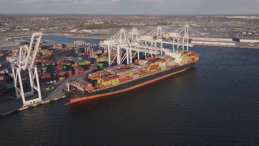 Loaded container ship sits at loading dock across water from warehouses