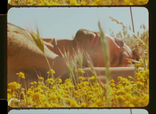 Man without shirt lying on the floor with yellow flowers around
