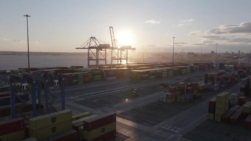 Aerial panorama of a port distribution center full of containers on the seafront with the sunrise on the horizon
