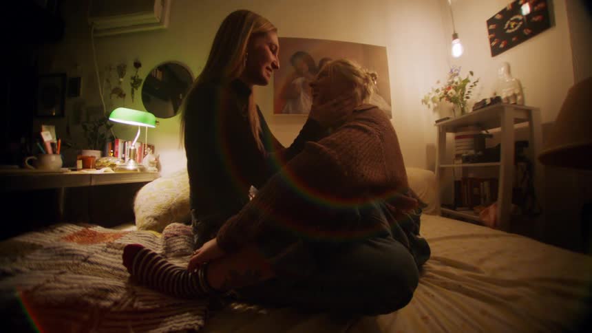 Two women hugging each other and sitting on the bed looking at each other and smiling affectionately