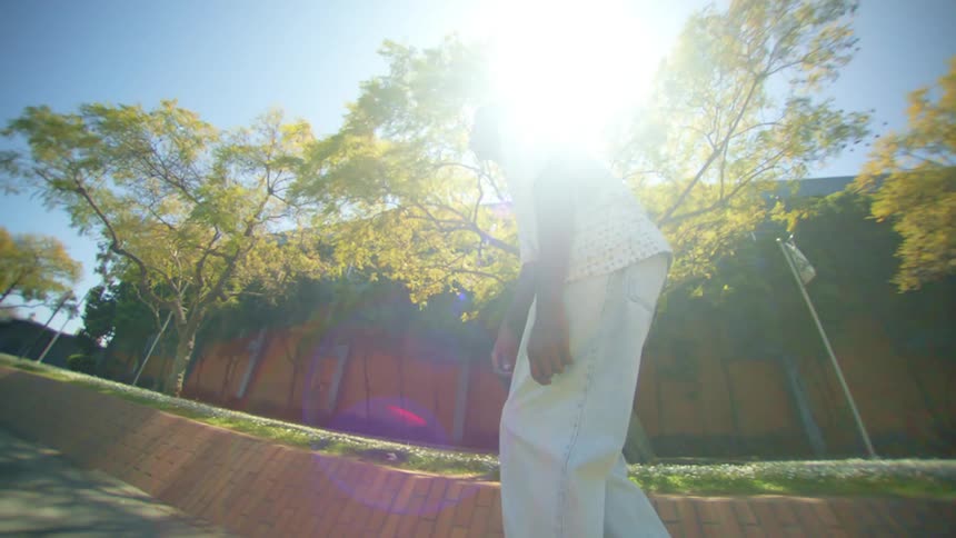 Man in jeans and shirt riding a skateboard on the sidewalk of a city with trees on the side