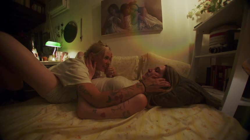 Woman lying down with her legs open and a woman on top stroking her hair in a romantic way