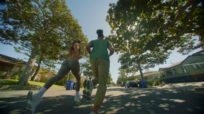 Two people are jogging on a sunny street lined with trees and houses