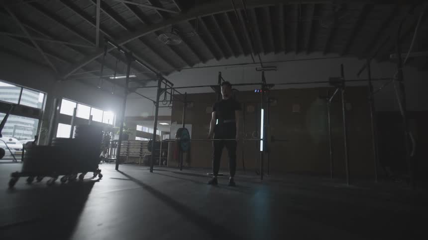 A man lifting a rod with two weights on the sides in a place full of iron trusses