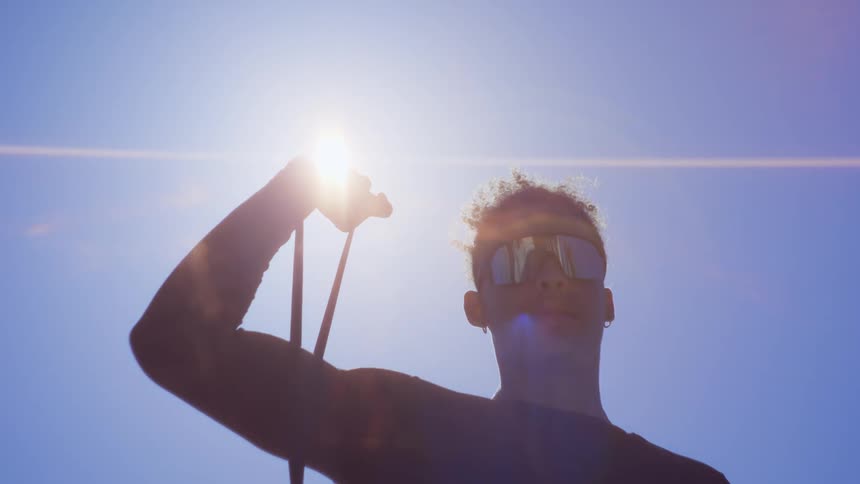 Young man in an openair environment with sunlight and sunglasses stretching one of his arms with an elastic band