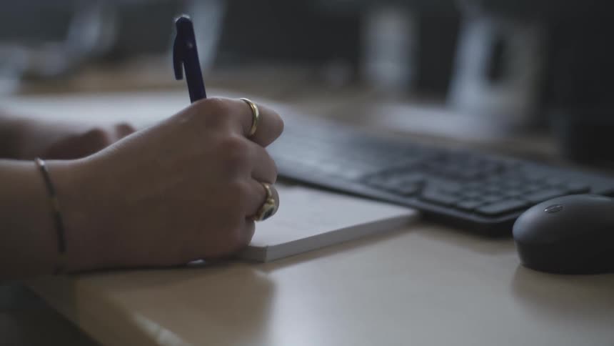 A woman writes a note and types on the keyboard