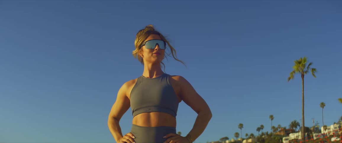 Woman with her hands on her hips wearing sunglasses while standing in an openair environment with palm trees around her