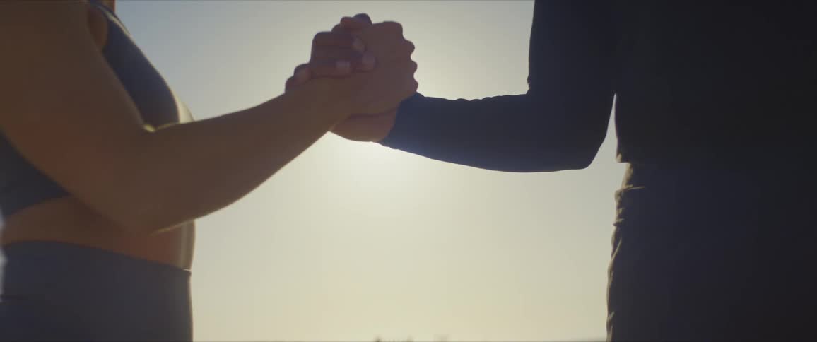 Man and woman shaking hands against a strong sun on the horizon