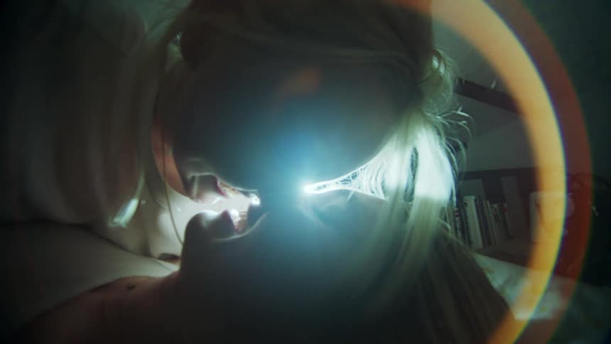Two women smile at each other then kiss lit by a glaring light