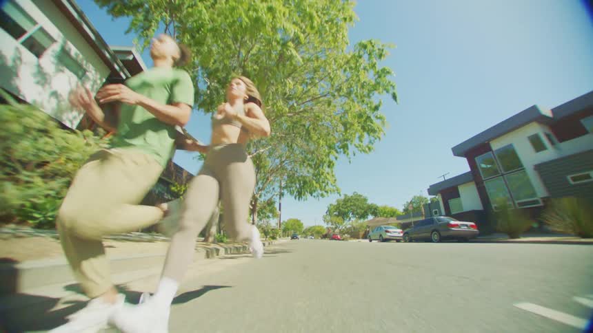 Two joggers run along the side of road through a residential neighborhood