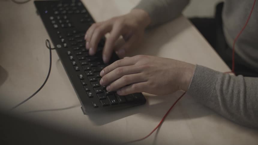 Hands of a man sitting at an office desk typing on a keyboard