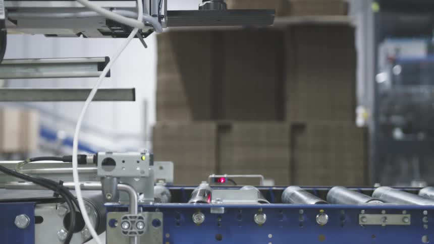 Cardboard box passing on a conveyor belt being stamped and in the background a worker passing by