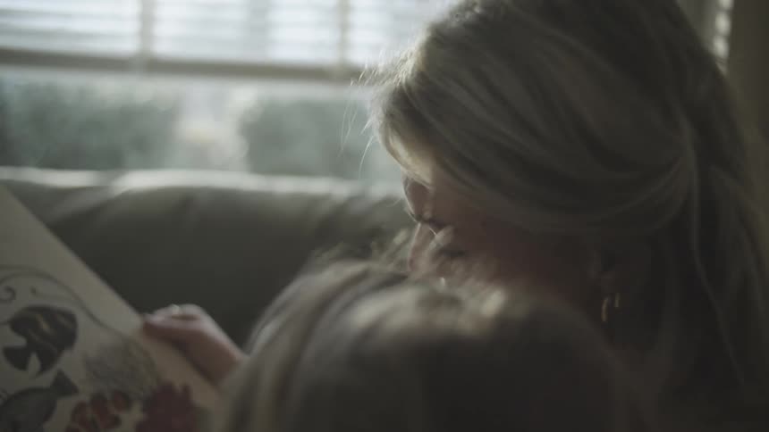 A blonde woman reading a childrens book to a blonde child who is next to her