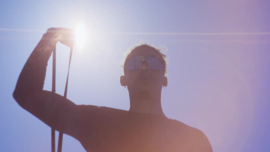 Sun glares down partially silhouetting man holding object in one uplifted arm