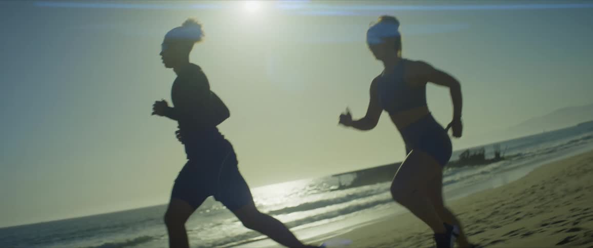 Man and woman with sunglasses running together side by side by the sea on the beach