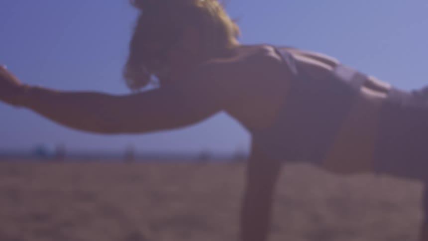 Woman squatting on the beach sand stretching her body