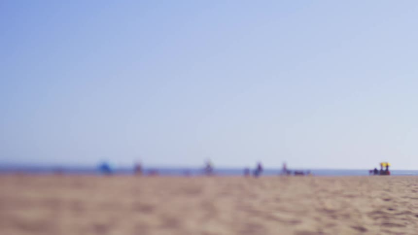 People riding their bikes as others sit in the sand on a beach on a bright sunny day
