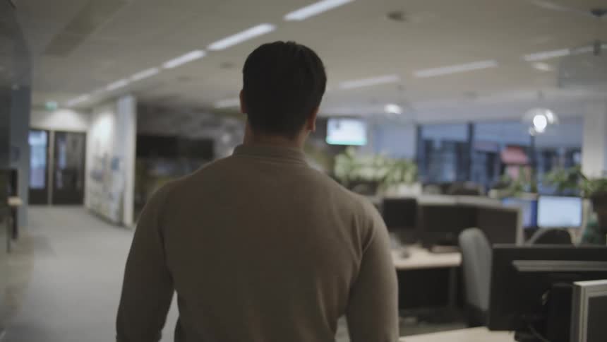 Back view of a man walking towards his desk in an office