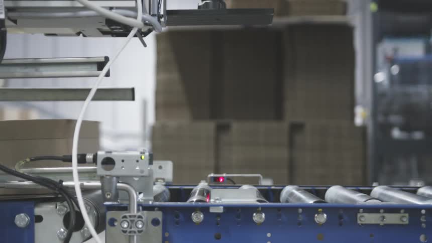 Interior of a factory with a box passing on a conveyor belt and being stamped by a machine