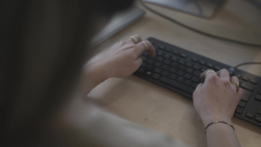 Hands of a blonde woman wearing headphones and she is typing on the black keyboard