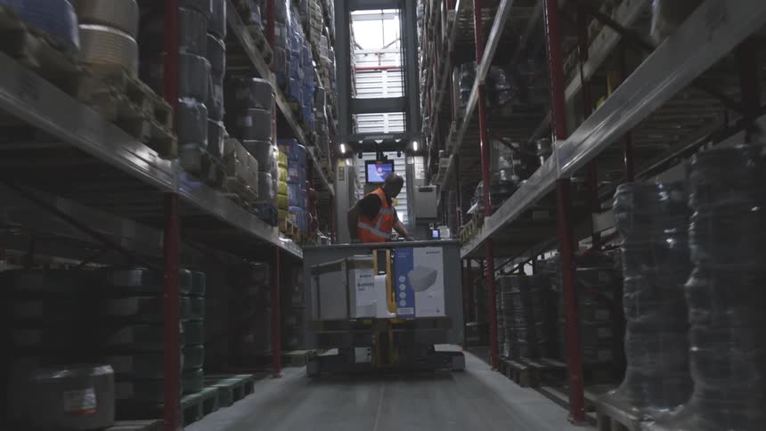 A man drives a forklift down a narrow corridor in a warehouse