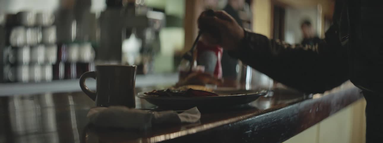 A person is seated at a restaurant with a plate of food and a mug eating lunch or breakfast