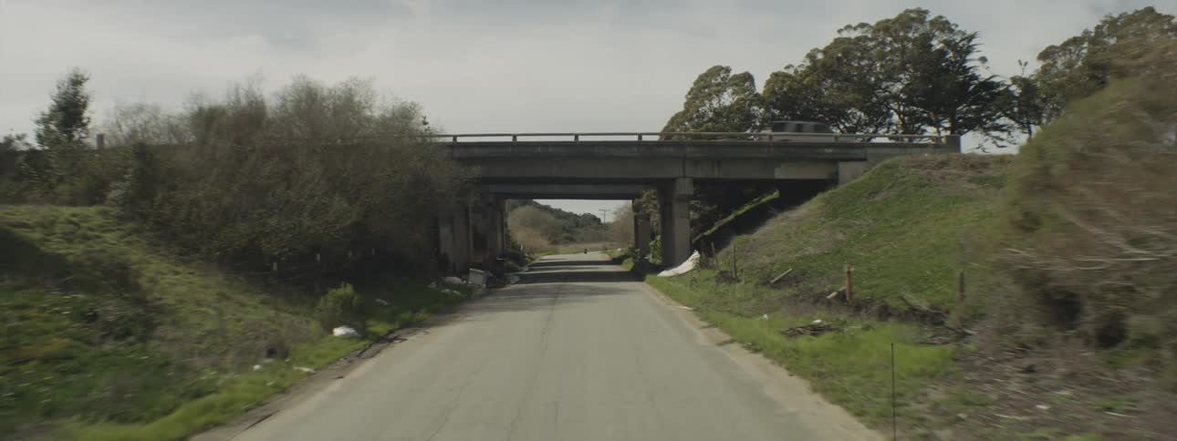 A small rural asphalt road that passes under a small bridge