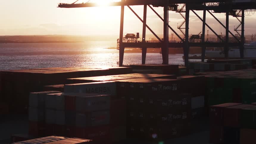 Logistics center with containers on the edge of the sea with an orange sunset on the horizon