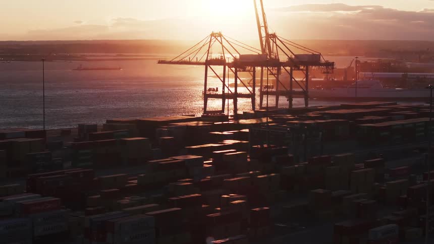 An aerial view of a harbor at sunset with container ships cargo cranes and colorful shipping containers stacked in rows
