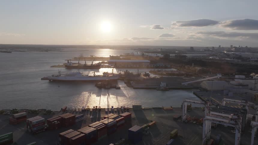 Aerial panorama of a port with containers on the seafront and cargo boats and the sun on the horizon