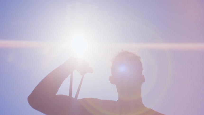 Portrait of a man wearing sunglasses and stretching his arm with a rubber band while standing in an open air environment