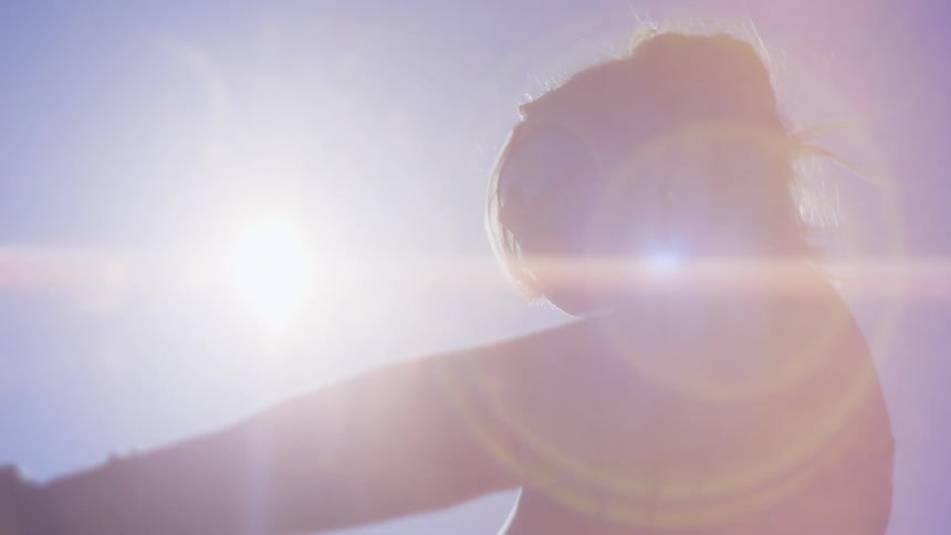 A young woman holds a black pole with the sun beaming down on her