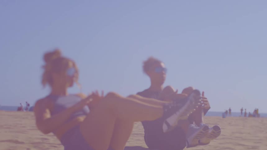 Two women are stretching on the beach