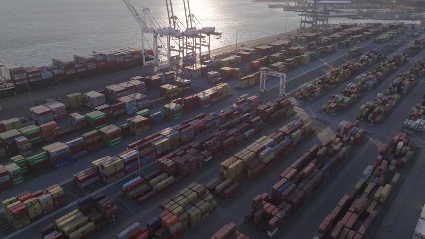 Container ship sits docked near loading cranes down coast from city on a misty day