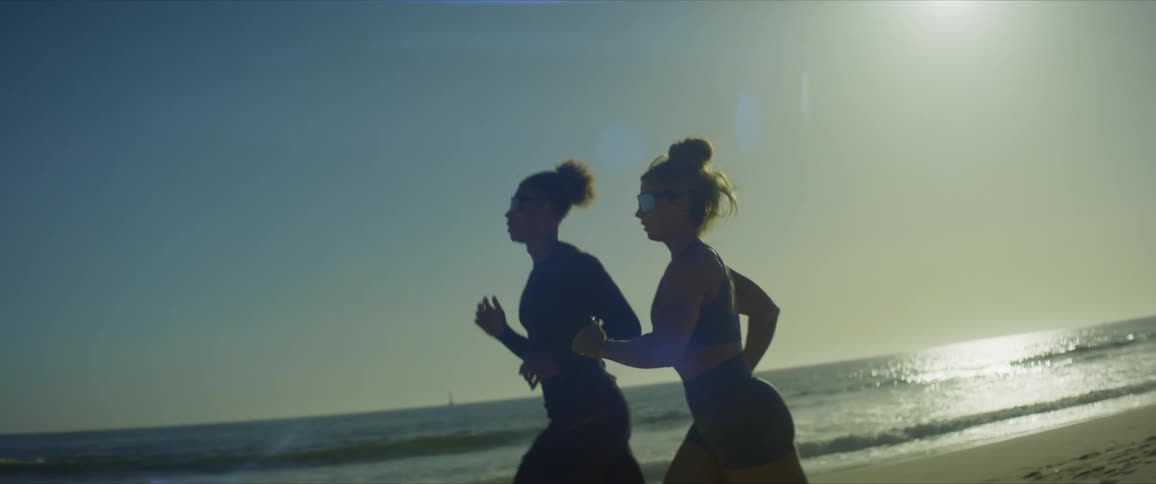 Man and woman running on the beach sand with sunglasses