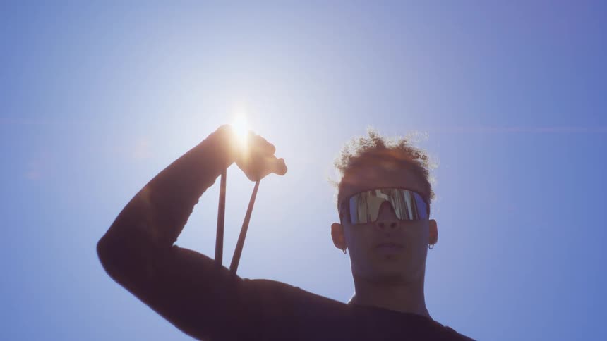 A young man exercises with a resistance band on his right arm on a sunny day