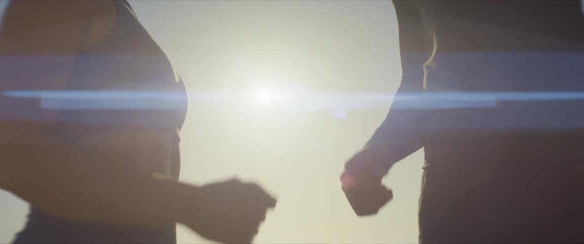 Two people fist bump with the sun shining behind them