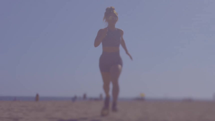 A woman in training clothes is running on the beach sand