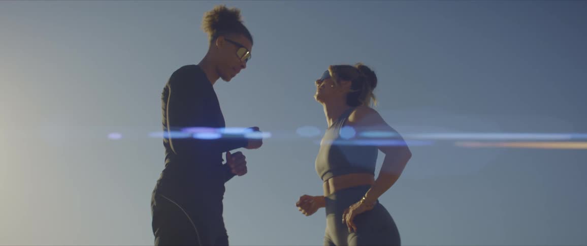 Two young fit people wearing sports clothes fist bump with a clear sky behind them