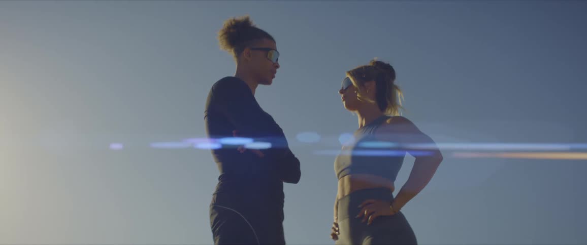A man and a woman wearing sunglasses and sports outfits stand against the blue sky