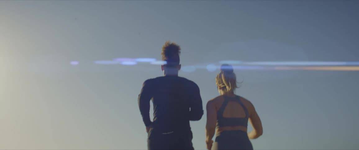 Back view of a man and woman running side by side on the beach on a summer day