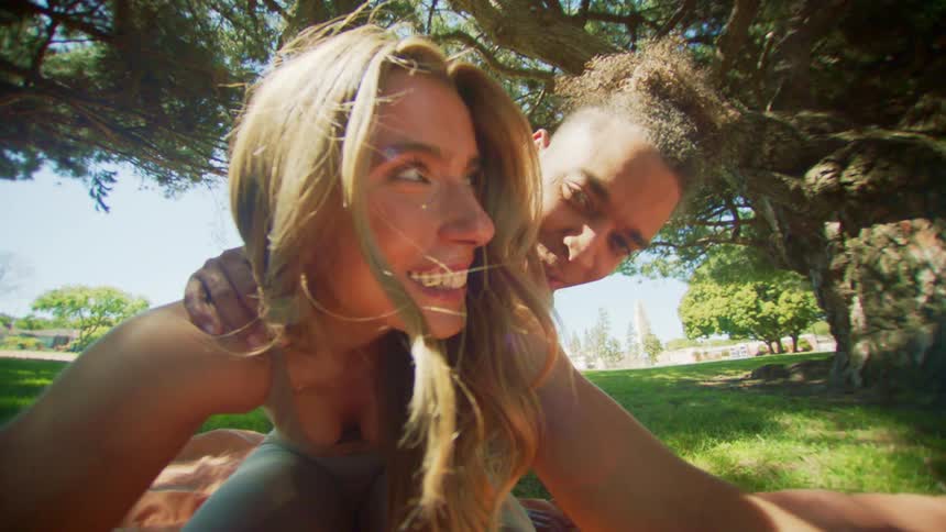 A woman wearing green sportswear stretches her legs with a man with curly hair in the green public park