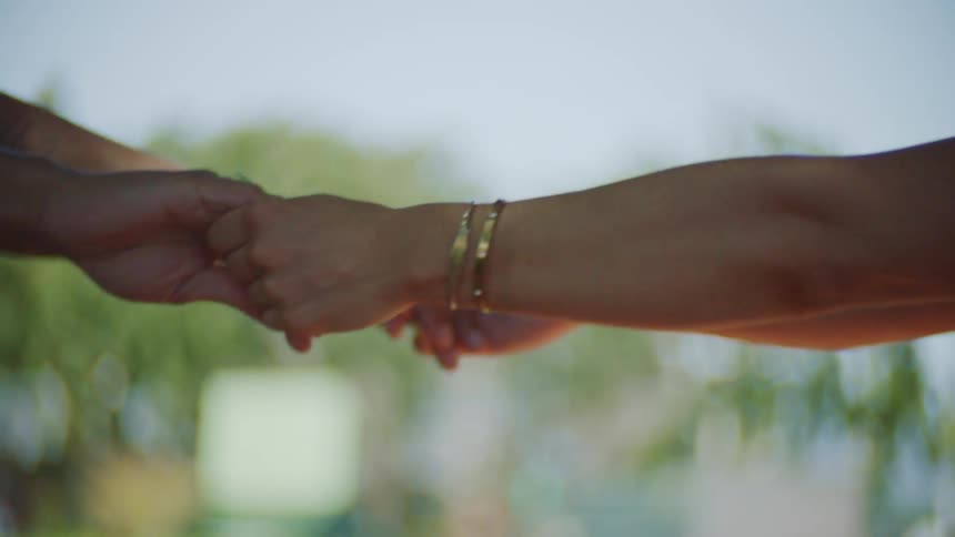 A couple holding hands one being led by the other the woman lowers her head